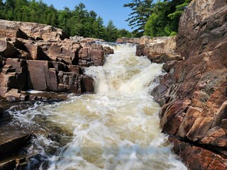 Rocky river rapids flowing through narrow gorge in summer. Fast and powerful river rapids flowing...