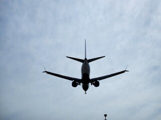 Airplane landing silhouette against cloudy sky. A commercial passenger jet captured from below while approaching the runway.