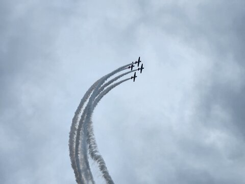Aerobatic formation performing a smoke trail loop in cloudy sky. A group of light aerobatic aircraft in tight formation, leaving curved trails during a dynamic display against a dramatic cloudy sky.