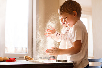 Happy children playing with flour while baking cookies in bright sunlight