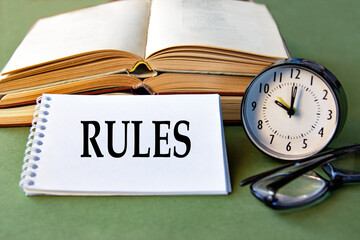 RULES text notebook with alarm clock, glasses and books on a green background