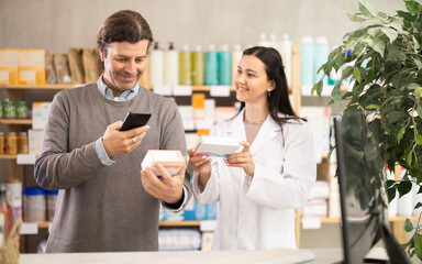 Adult man buyer scanning qr code for box of pills with adult woman pharmacist in pharmacy