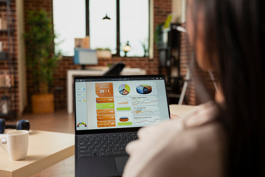 Female manager works remotely, reviewing business analytics on laptop. Asian female entrepreneur updating financial charts and data while managing startup projects from home office.