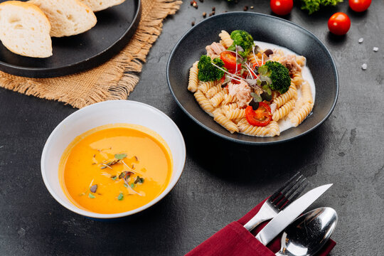 Creamy fusilli with tuna, broccoli and cherry tomatoes, served with soup on dark table