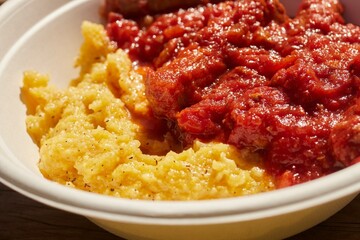 Polenta with a tomato and sausage sauce served in a disposable bowl as served in Rifugio Velasco, an Italian Alpine mountain hut.