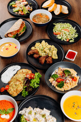 Overhead flat lay of assorted restaurant dishes, soups and salads on wooden table