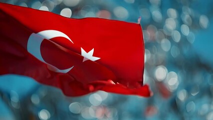 Red flag of Turkey waving in wind with moon and star symbol. Turkish national pride and independence symbol against blue sky.