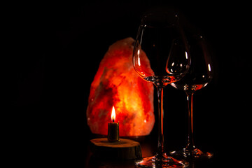 Two elegant empty clear wineglasses for red wine on the table with burning candle on dark black background with blur orange salt lamp. Closeup decor celebration