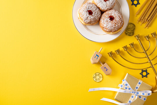 Vibrant Hanukkah scene featuring donuts on a plate, a menorah, a dreidel, and wrapped gifts on a bold yellow backdrop conveying festive spirit and tradition
