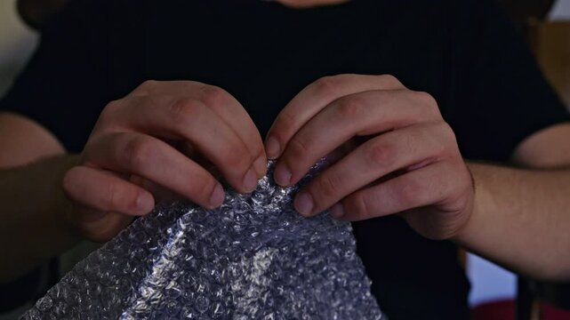 Hands engage in the simple, yet satisfying activity of popping bubble wrap. This clear plastic packaging material offers a playful and effective way to relieve stress and reduce anxiety.