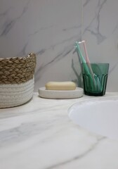 A clean and minimalist bathroom scene: the composition includes a toothbrush holder with toothbrushes, a bar of soap, woven basket