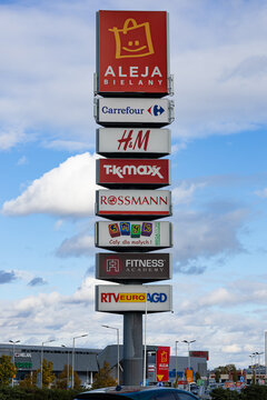 Wroclaw, Poland- October 25, 2025: Vertical signpost for Aleja Bielany Shopping Center, listing major retail tenants like Carrefour, H and M, TK Maxx, and Rossmann against a bright, cloudy sky