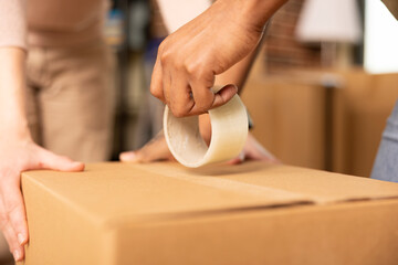 Close up of male hands sealing cardboard box using adhesive tape, getting ready to move out....