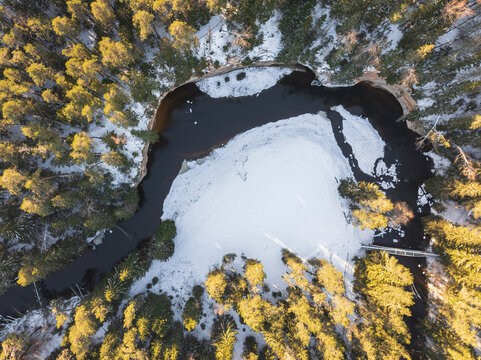 Aerial top-down drone view of meandering Ahja River and snowy forest in Taevaskoda, Estonia during golden hour sunset. - Powered by Adobe