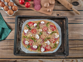 Step 15. Raw pizza with fresh ingredients in one baking dish on a wooden table.