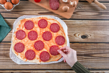 Step 8: The woman's hands place the sausage on the dough on a wooden table.