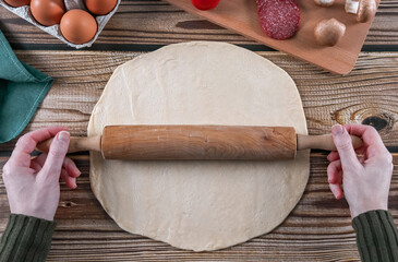 Step 6: A woman's hands roll out thin dough on a wooden table.