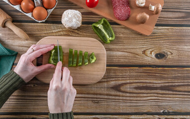Step 10: Woman's hands cutting peppers for pizza dough on a wooden table.