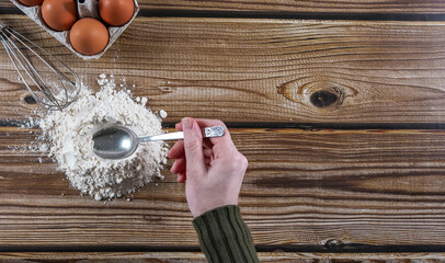 Step 2: A woman's hand makes a hole in the flour with a spoon on a wooden table.