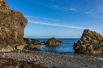 Sunny coastal cove with large jagged rock formations and pebble beach in the Isle of Man.