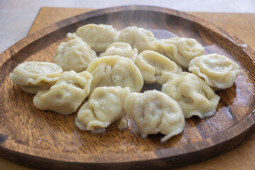 Steaming homemade dumplings served on rustic wooden plate closeup