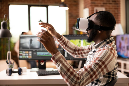 Creative individual with raised hands, using vr editing software to streamline and arrange footage. Black man seated home office desk, producing cinematic content with immersive virtual reality tools.