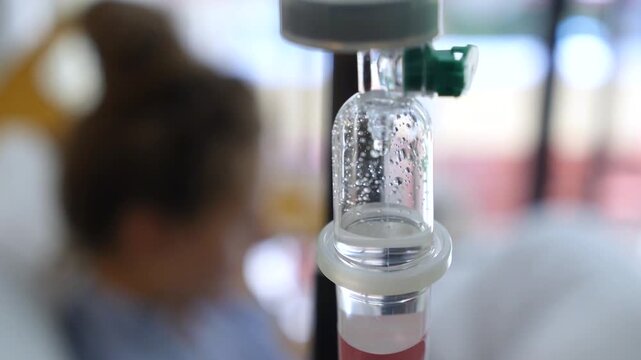 Medical iv drip chamber administering medication or saline solution to an out of focus patient resting in a hospital bed, a crucial element in modern healthcare and recovery treatments