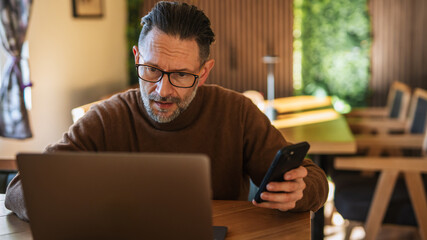 Mature man working remote using laptop and phone