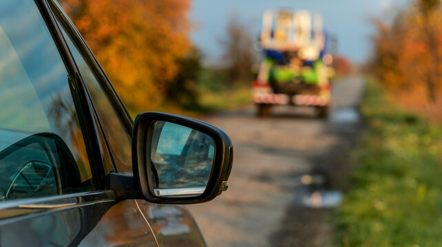 Car side mirror view of a truck on a rural road in autumn