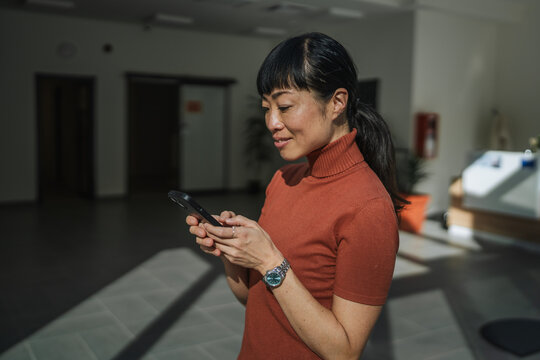 Asian woman smiling using smart phone in modern workspace