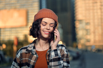 Fototapeta premium Woman phone smile urban beanie golden hour candid lifestyle portrait of a young woman on a phone in warm sunlight, authenticity and emotional storytelling with mindful living golden glow.