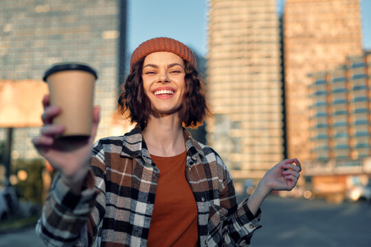 woman coffee smile urban golden candid lifestyle beanie joyful portrait of a woman offering a takeaway cup in warm golden hour glow, authenticity and mindful living in emotional storytelling moment