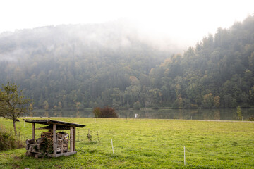 Foggy morning in the meadow with wooden hut in the foreground