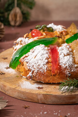 Colorful candied fruits and powdered sugar on a traditional Bolo Rei or Kings Cake, set on a wooden board amidst warm holiday decorations and lights. Is tradicional for Christmas in Portugal