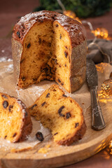 A delicious Panettone with raisins, partially sliced to reveal its moist interior, dusted with powdered sugar and presented on a wooden board with a silver knife