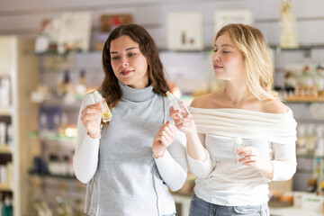 Young woman seller offers to test fragrances to young woman buyer in perfume shop