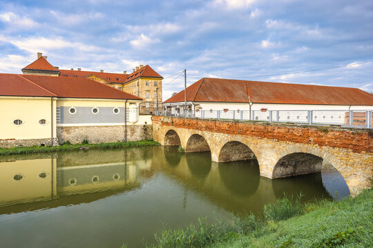 Holic, Slovakia - October 12, 2024: The Holic castle. Picturesque view of a stone bridge reflecting in the calm river water, with the buildings under a cloudy sky creating a serene landscape.