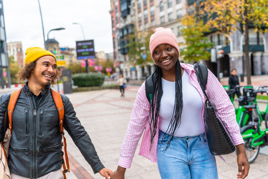 Diverse couple walking outdoors holding hands in city