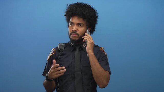 African american man in police uniform using smartphone against isolated blue wall background.