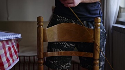 A man carefully measures the dimensions of a wooden chair with a yellow tape measure, focusing on precision for a home improvement project or furniture assessment.