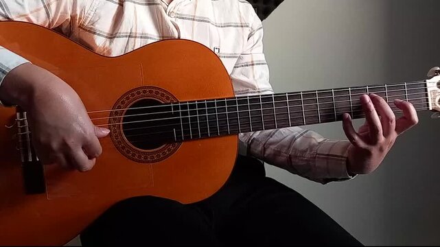 A man playing tremolo fingerstyle technique with classic guitar and changing notes on the fretboard  with his left hand from a forward angle near sunset