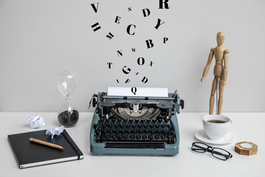 Vintage typewriter with cup of coffee, wooden mannequin and notebook on white table near wall