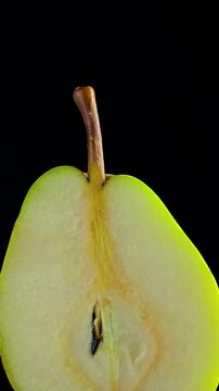 Vertical video of a fresh pear half displayed on a dark black background with detailed view of pulp, seeds and skin. Concept related to fruit, vitamins, vegetarian nutrition, cooking ingredients