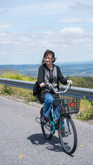 Smiling Asian teen girl cycling on countryside road with wind turbines.