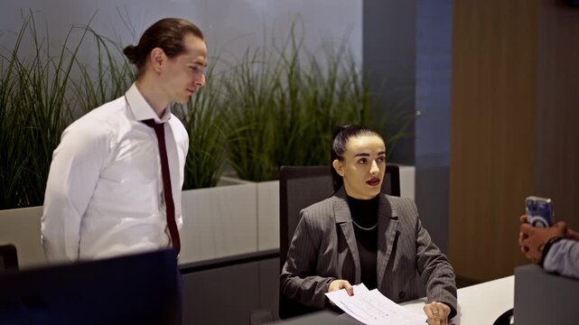 Two professional business colleagues engage in a focused discussion, reviewing important documents at a modern office desk. Their interaction highlights effective teamwork and productivity.