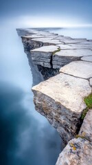 A dramatic stone path made of large, flat rocks leads precariously over a cliff edge into a misty, blue abyss.