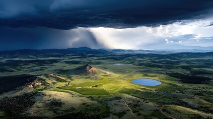 A dramatic aerial view captures a vast, rolling green landscape under a dark, stormy sky, with sunlight breaking through to illuminate a lake and a central hill