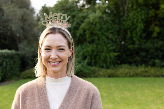 Mid adult woman posing in private garden wearing metallic Merry Christmas headband and cardigan