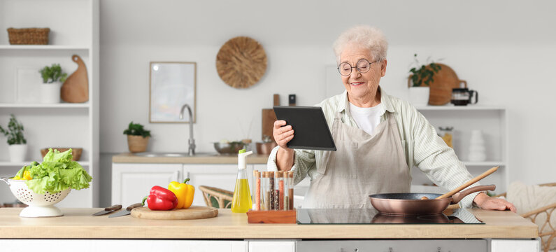 Senior woman with tablet computer frying vegetables in kitchen