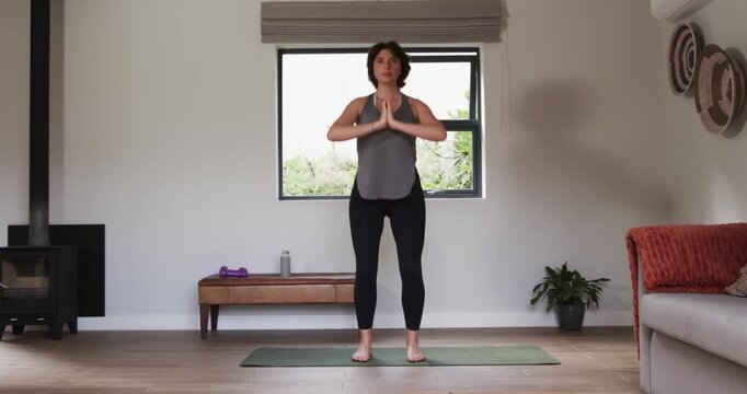 Woman pressing palms together on yoga mat starting routine sumo squats alternating lunges at home